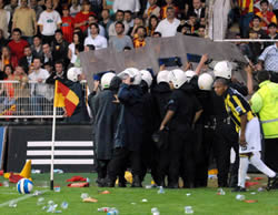 Police protect Fenerbahce player from a hail of missiles while he takes a corner